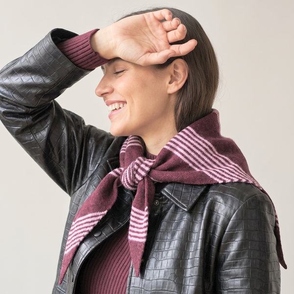 A woman wearing a dark burgundy knit triangle scarf with white stripes tied around her neck, styled with a black textured leather jacket over a matching burgundy ribbed top, against a plain light beige background.